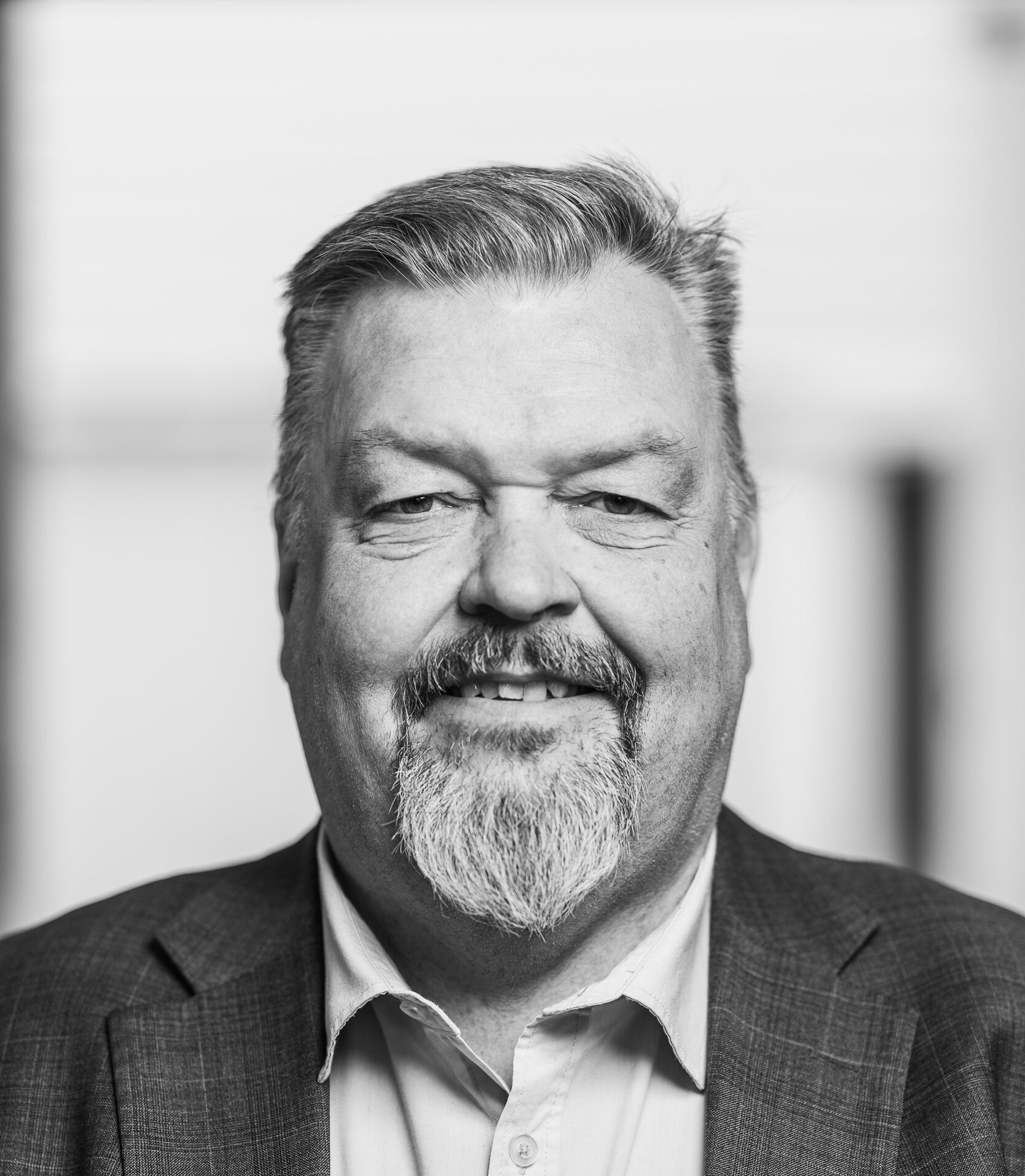 En man med skägg ler mot kameran, iklädd en kavaj och skjorta.