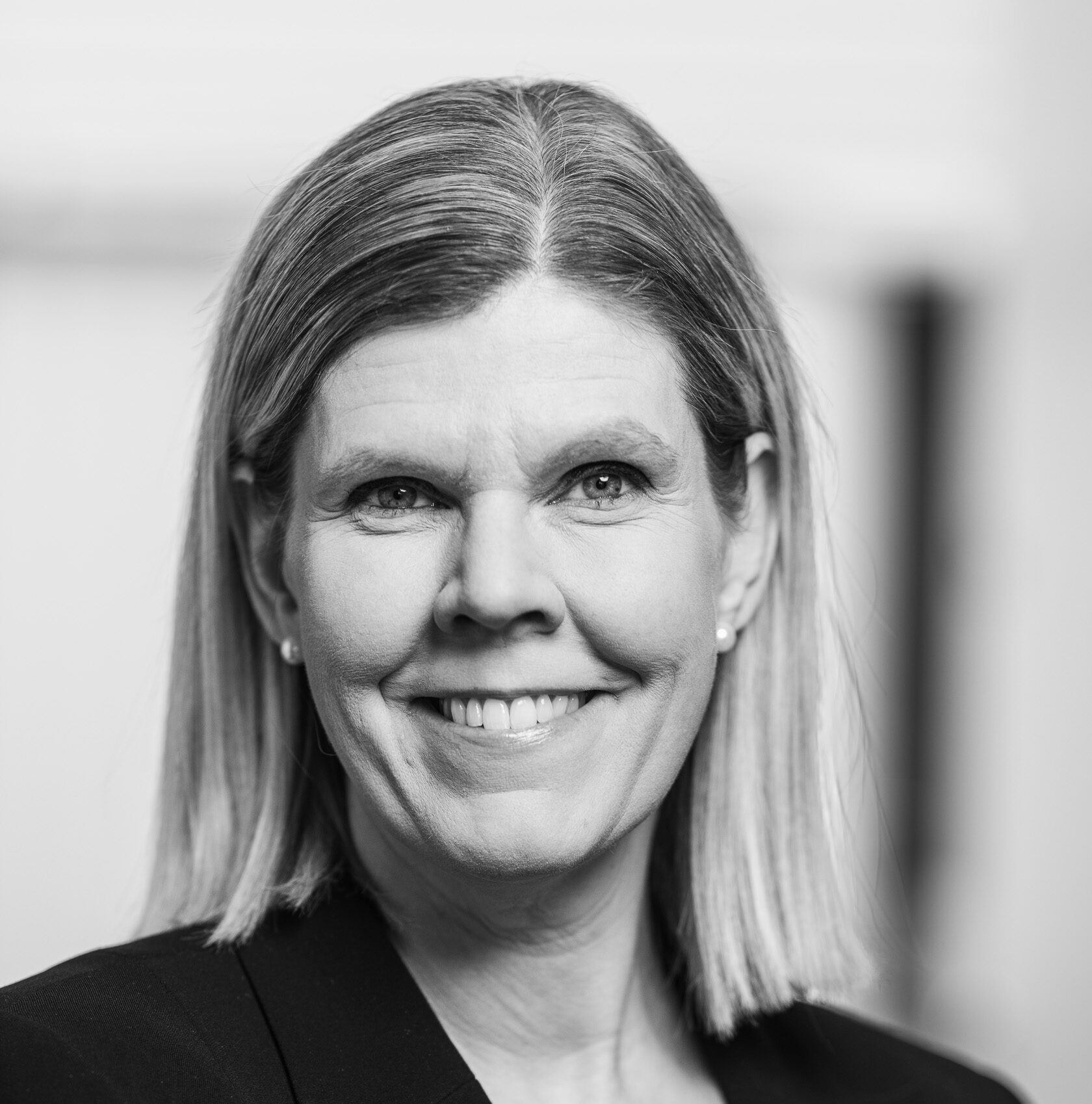 En kvinna med axellångt hår ler mot kameran, iklädd en kavaj.