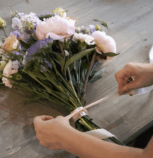En person binder en bukett med blommor med ett band.