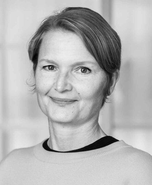 En person med kort hår ler mot kameran i en svartvit bild.