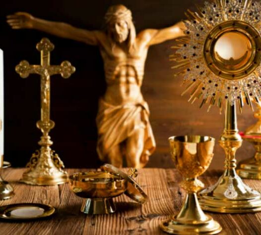 Kors, monstrans och kalkar i guld på ett träbord, med en bakgrund av en staty av Jesus på korset.
