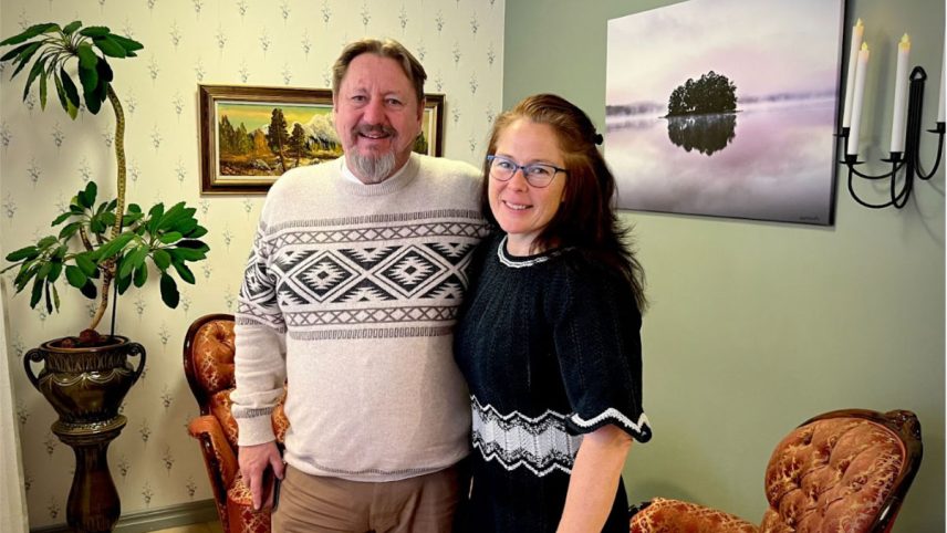 En man och en kvinna står leende i ett rum med klassisk inredning, omgivna av växter och tavlor på väggarna.