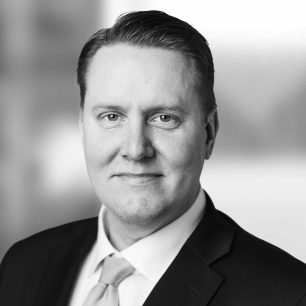 A black and white portrait of a man in a suit and tie, smiling slightly, with a blurred background.