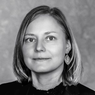 A grayscale portrait of a woman with shoulder-length hair, wearing a dark top and large, leaf-shaped earrings, looking directly at the camera.