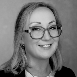 A person with glasses smiles warmly, looking towards the camera in a black and white portrait.