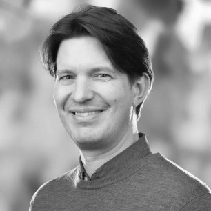 A person with short hair smiling, wearing a sweater, in a grayscale portrait.