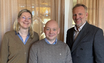 Three people standing together indoors, smiling at the camera.