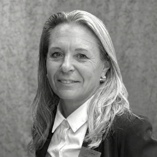 A woman with long hair smiles, wearing a suit and a name tag against a textured background.