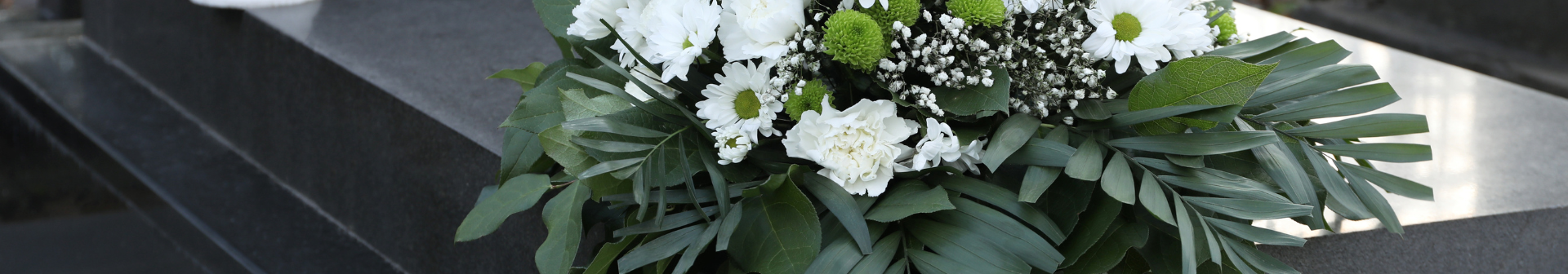 A bouquet of white and green flowers, including daisies and chrysanthemums, rests on a dark granite tombstone.
