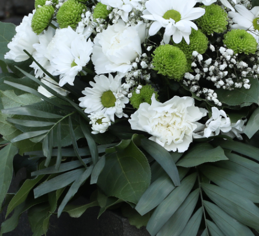 A bouquet of white and green flowers, including daisies and chrysanthemums, rests on a dark granite tombstone.