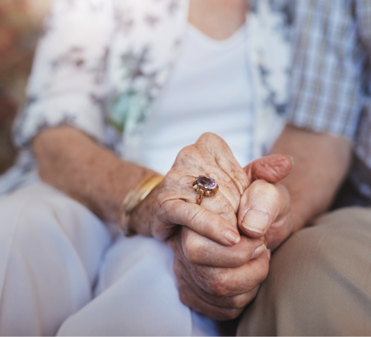 Elderly couple holding hands, one wearing a ring with a large gemstone.